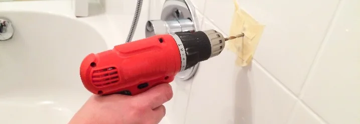 Hand bohrt mit einem Akkuschrauber in eine Fliese